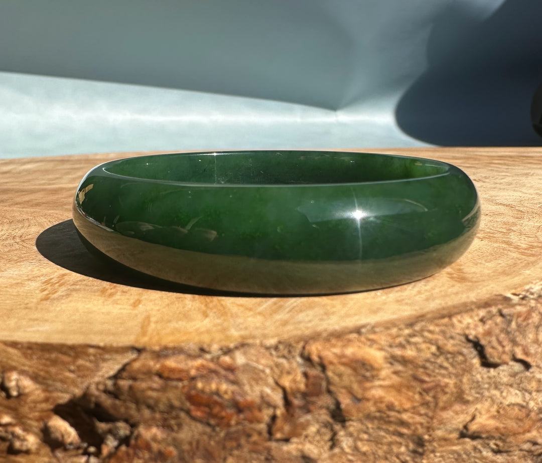 Side view of a glossy green nephrite jade bangle resting on a wooden surface