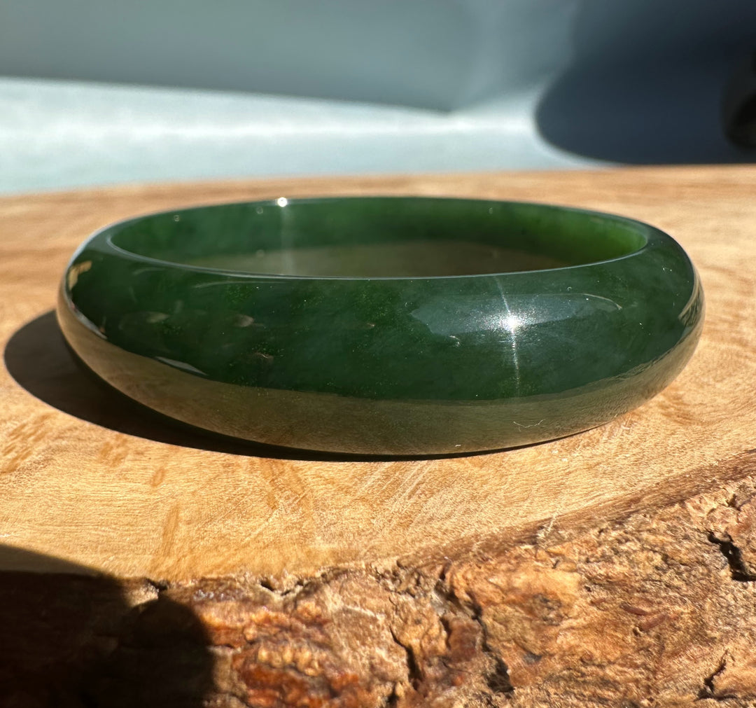 Canadian nephrite jade bangle 54 x 13.5mm in deep green with a glossy polished finish on wood
