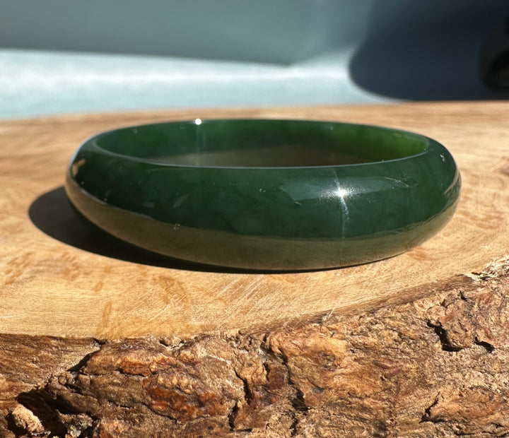 Dark green nephrite jade bangle with a polished surface resting on a wooden surface