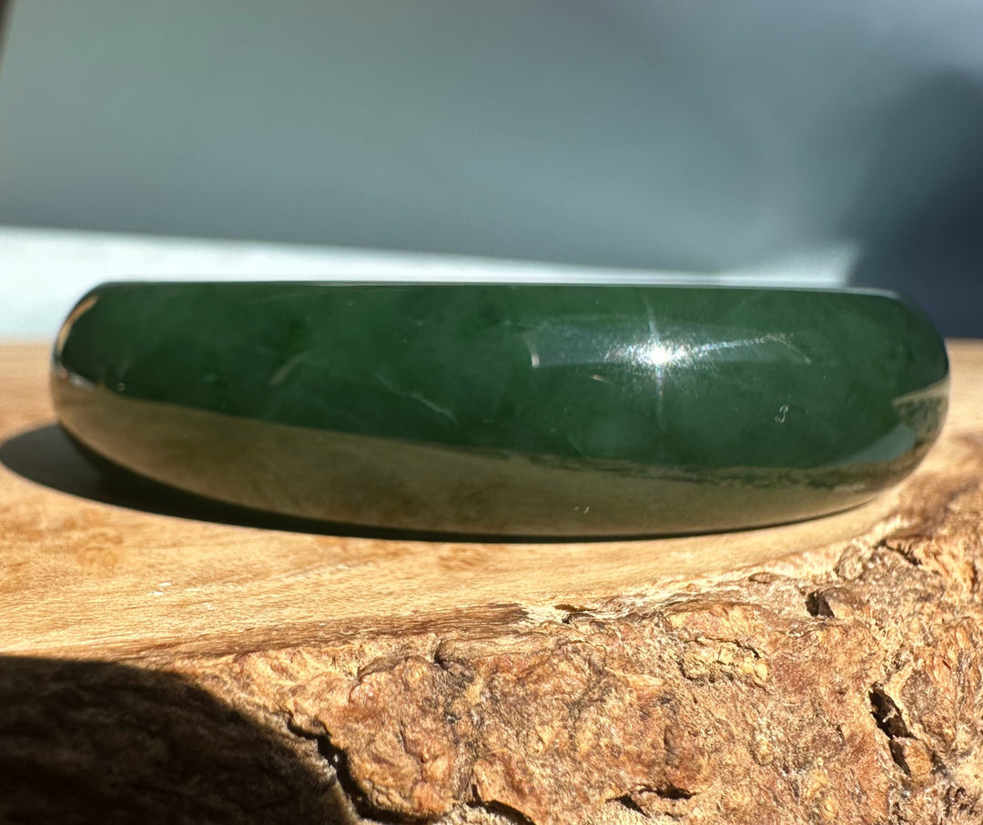 Bright green translucent nephrite jade bangle on a sunlit wooden surface