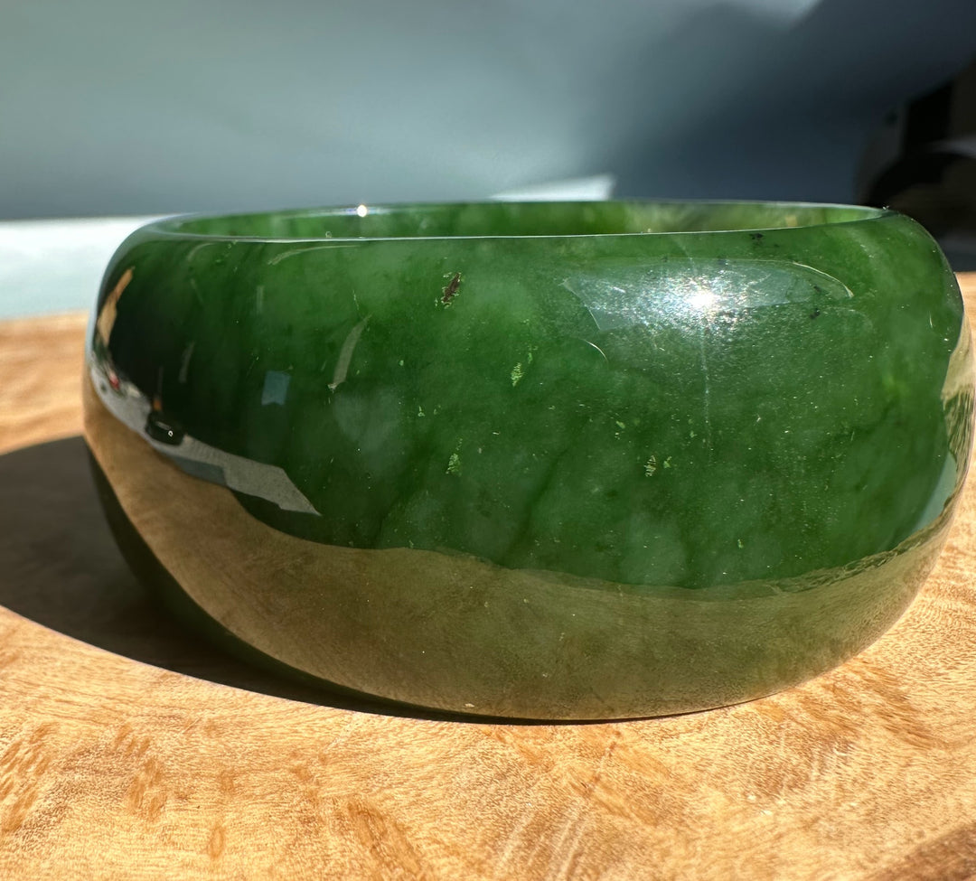Wide Cassiar Jade Bangle with dark green upper surface and beige mid band on a wooden surface