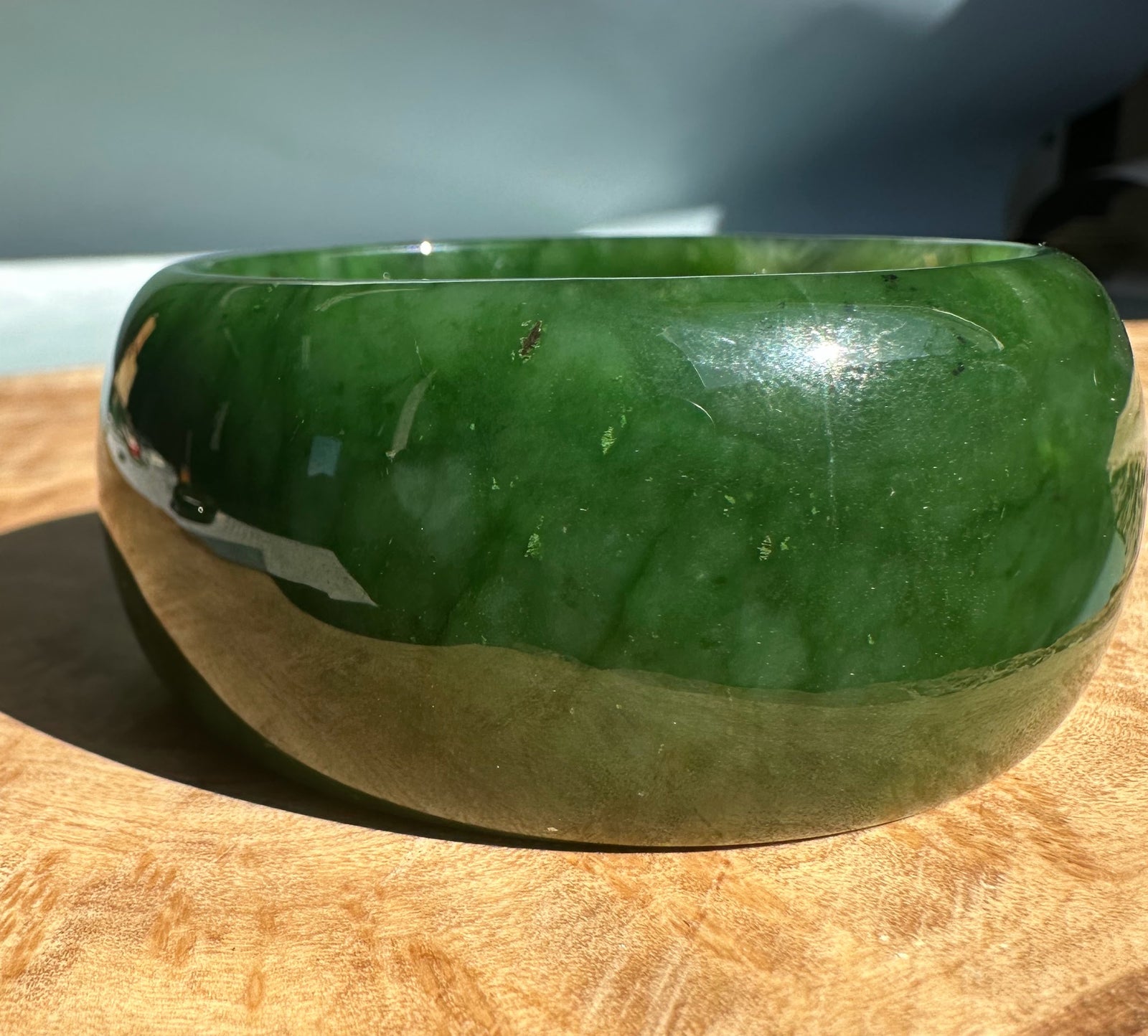 Wide Cassiar Jade Bangle with dark green upper surface and beige mid band on a wooden surface