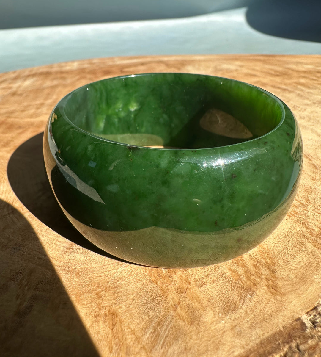 Wide Cassiar Jade Bangle with deep green color and glossy finish placed on a wooden surface