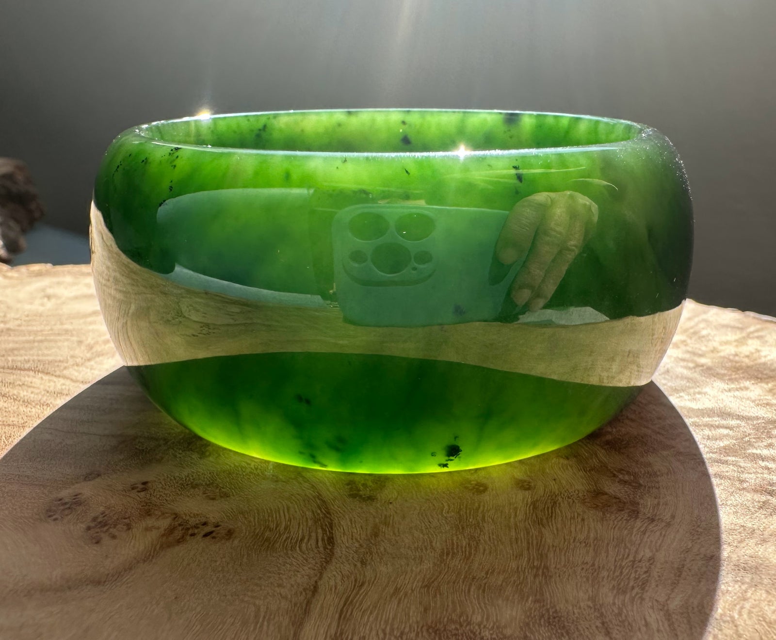 Wide Cassiar Jade Bangle in bright green with a natural tan wood band around the middle on a wooden surface
