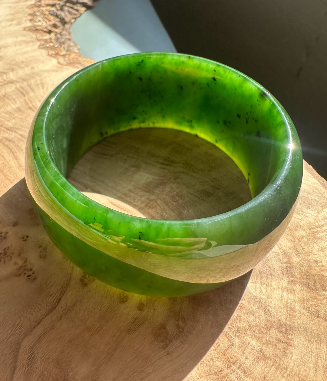 Wide Cassiar Jade Bangle with vivid green translucent jade and a pale cream band on a wooden surface.