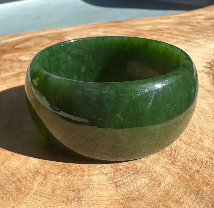 Angled top view of Wide Cassiar Jade Bangle showing rich green jade and a light band around the middle.