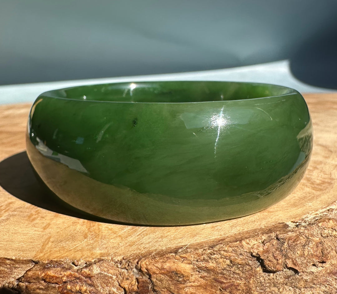 Wide Cassiar Jade Bangle 54 x 23.5mm dark green polished jade shown on a wooden log base