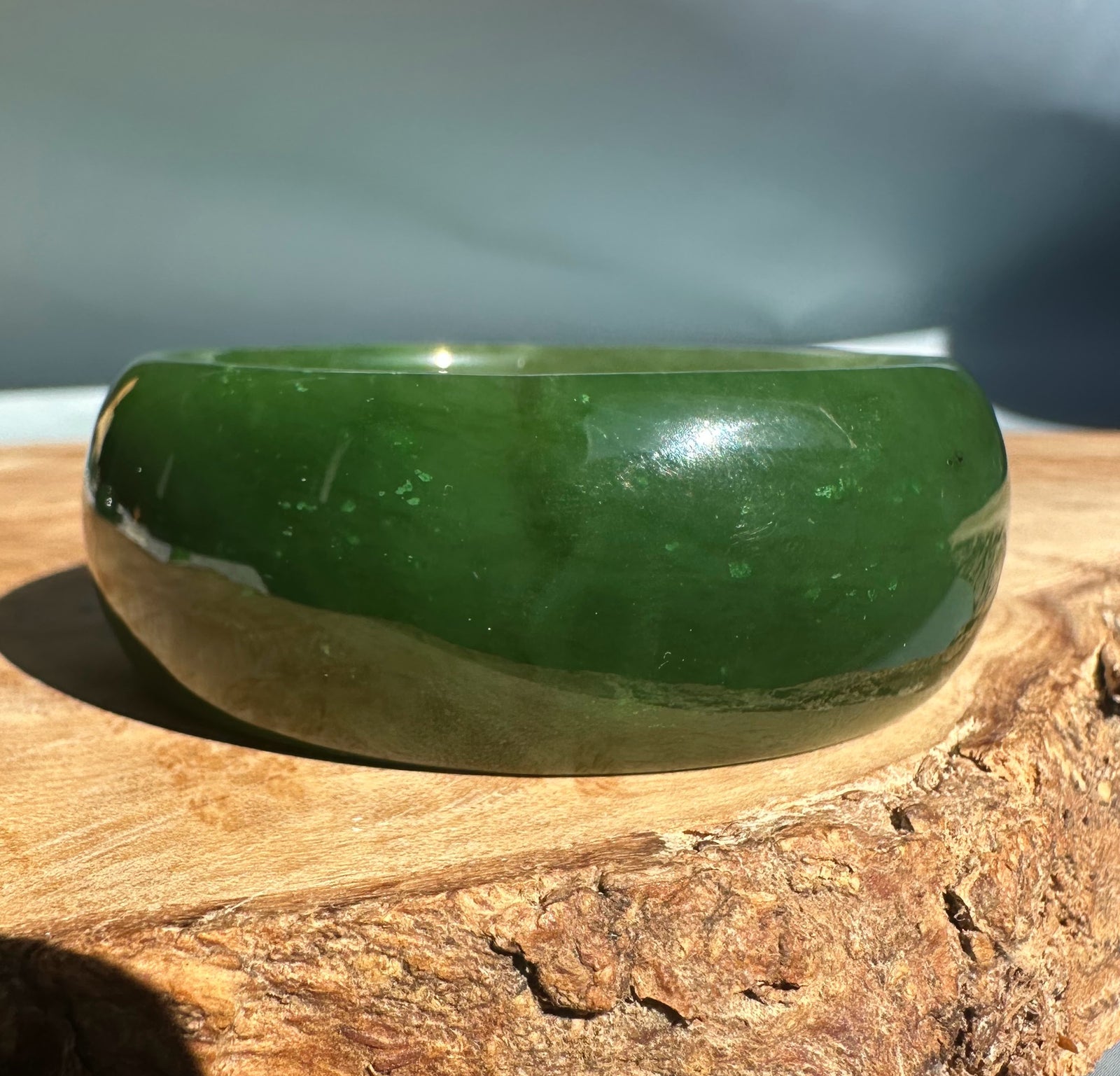 Wide Cassiar Jade Bangle 54 x 23.5mm in rich green resting on wood with a rounded polished exterior