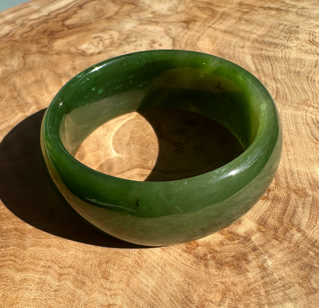 Top view of a thick jade bangle showing a rounded edge and vivid green color on wood