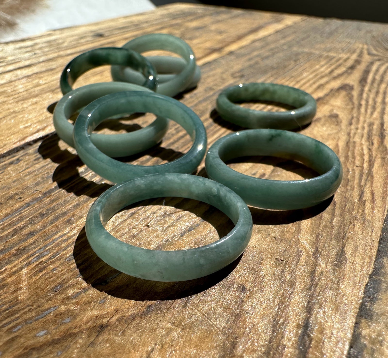 Group of narrow Guatemalan jadeite band rings in pale green on a wooden surface.
