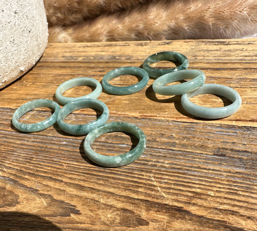 Narrow Guatemalan jadeite band rings in soft green tones on a wooden surface