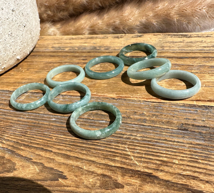 Narrow Guatemalan jadeite band rings in soft green tones on a wooden surface