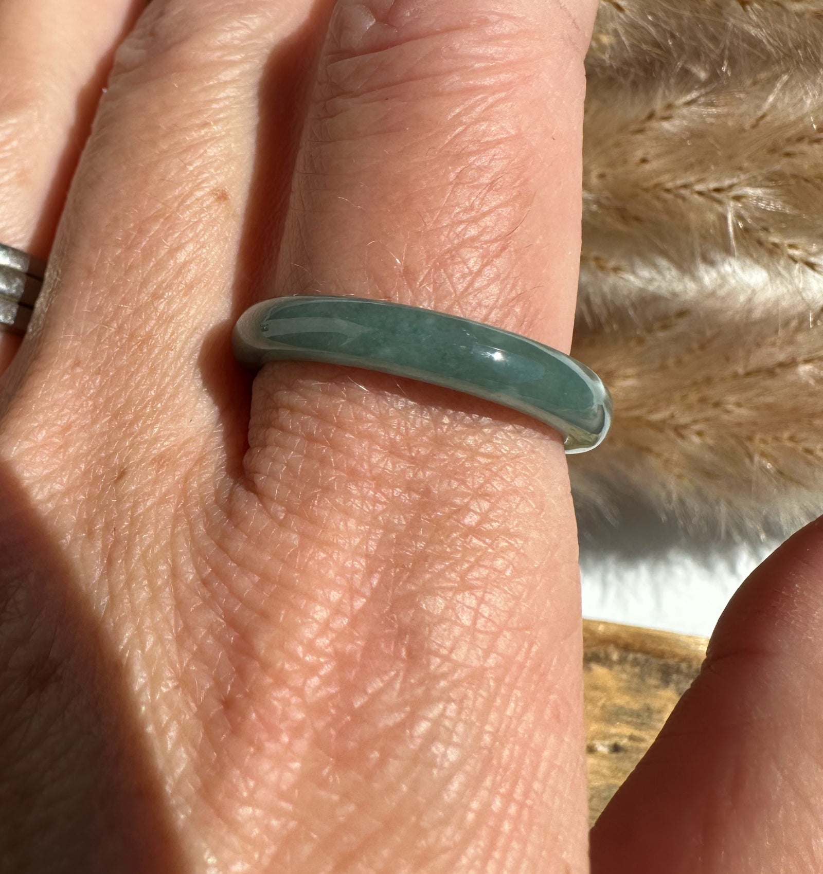 Close-up view of a pale-green jadeite narrow band ring worn on the finger.