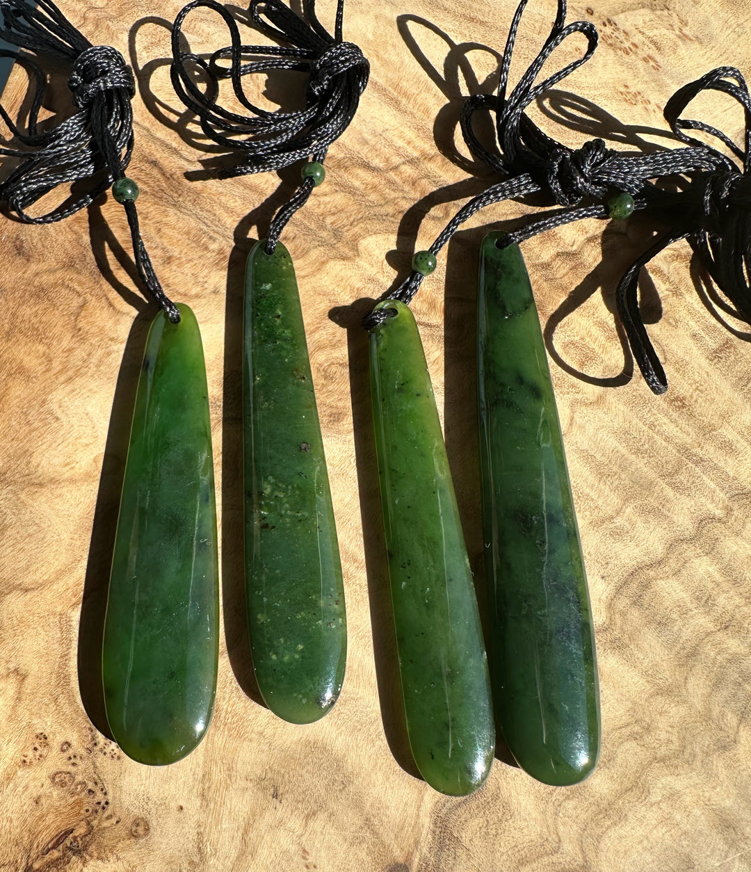Four long jade pendant drops on black cords with knotted loops