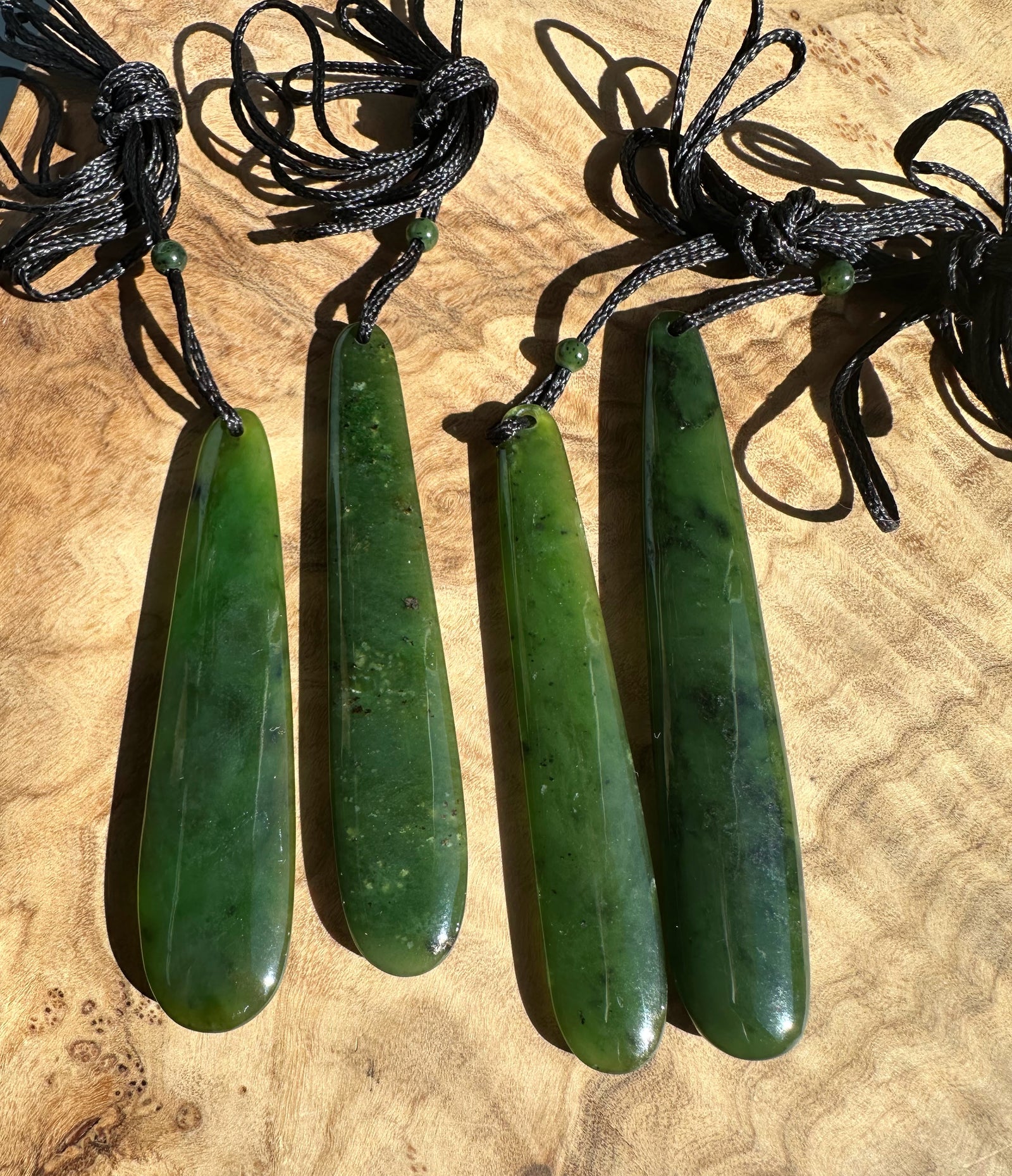 Four long jade pendant drops on black cords with knotted loops