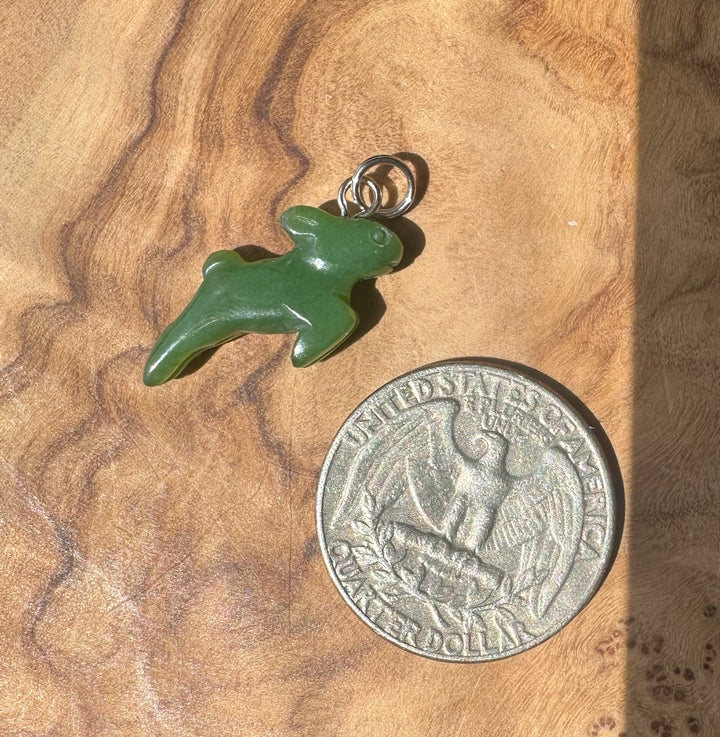 A small green carved animal-shaped charm or pendant with a metal loop at the top, placed on a wood surface next to a U.S.