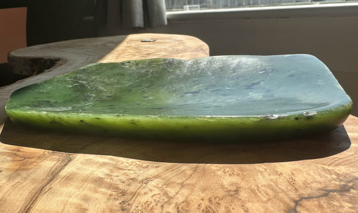 A green jade slab with a polished, smooth surface, displayed on a rustic wooden table in natural light.