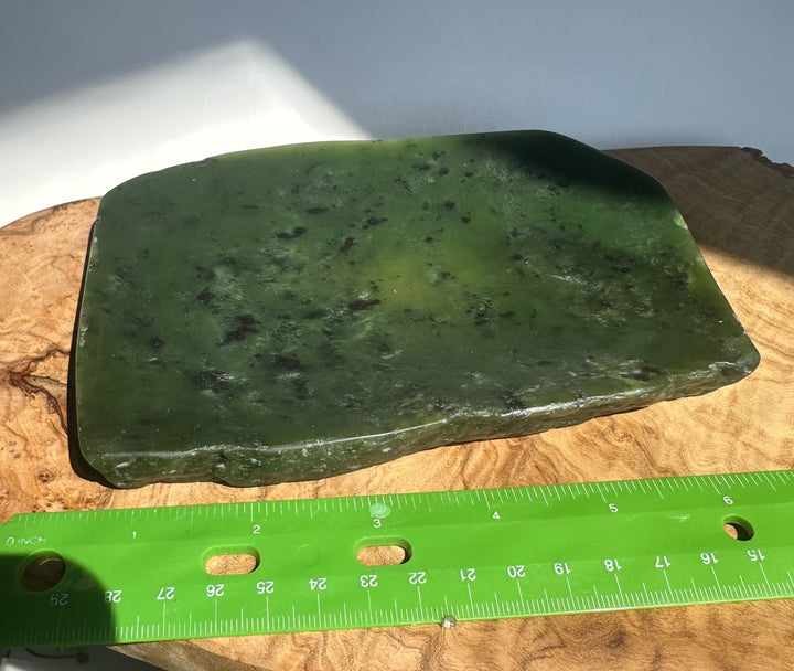 A green polished jade rectangular slab with natural speckling, displayed on a wooden surface next to a green measuring ruler for scale.