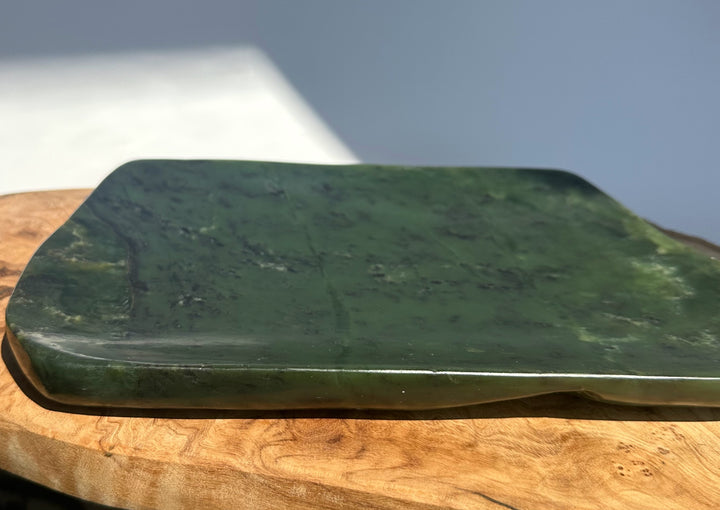 A polished dark green stone serving board with rounded corners, resting on a natural wood slice against a light gray background.