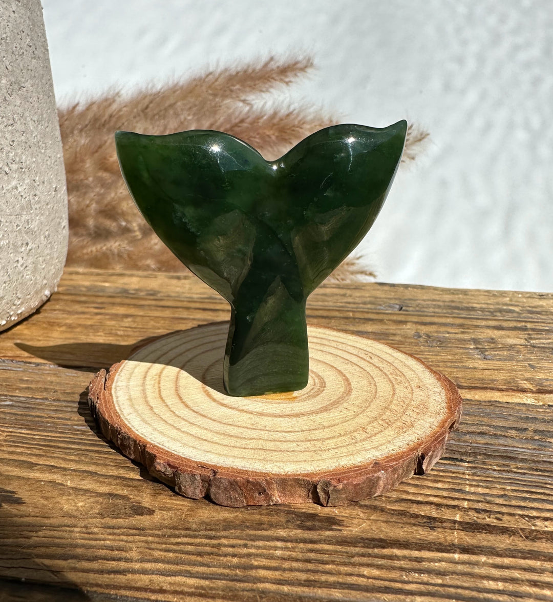 Deep green jade whale tail on a round wood base viewed from the side.