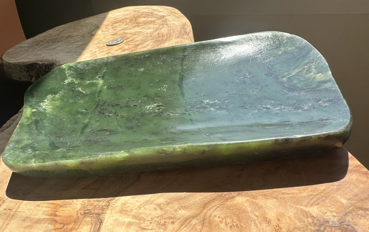 A polished green stone tray with a smooth, rounded rectangular shape, resting on a rustic wooden surface.