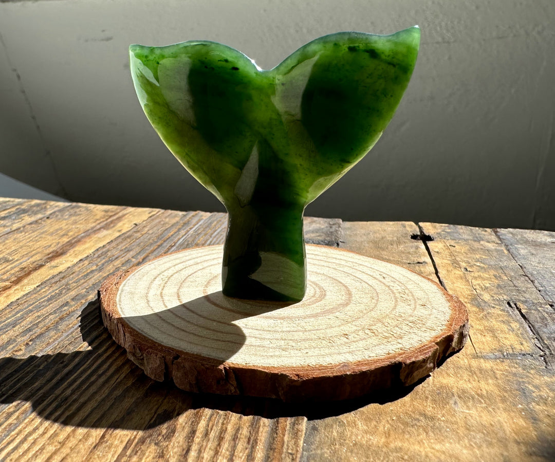 Jade whale tail sculpture in deep green mounted on a round wood base.