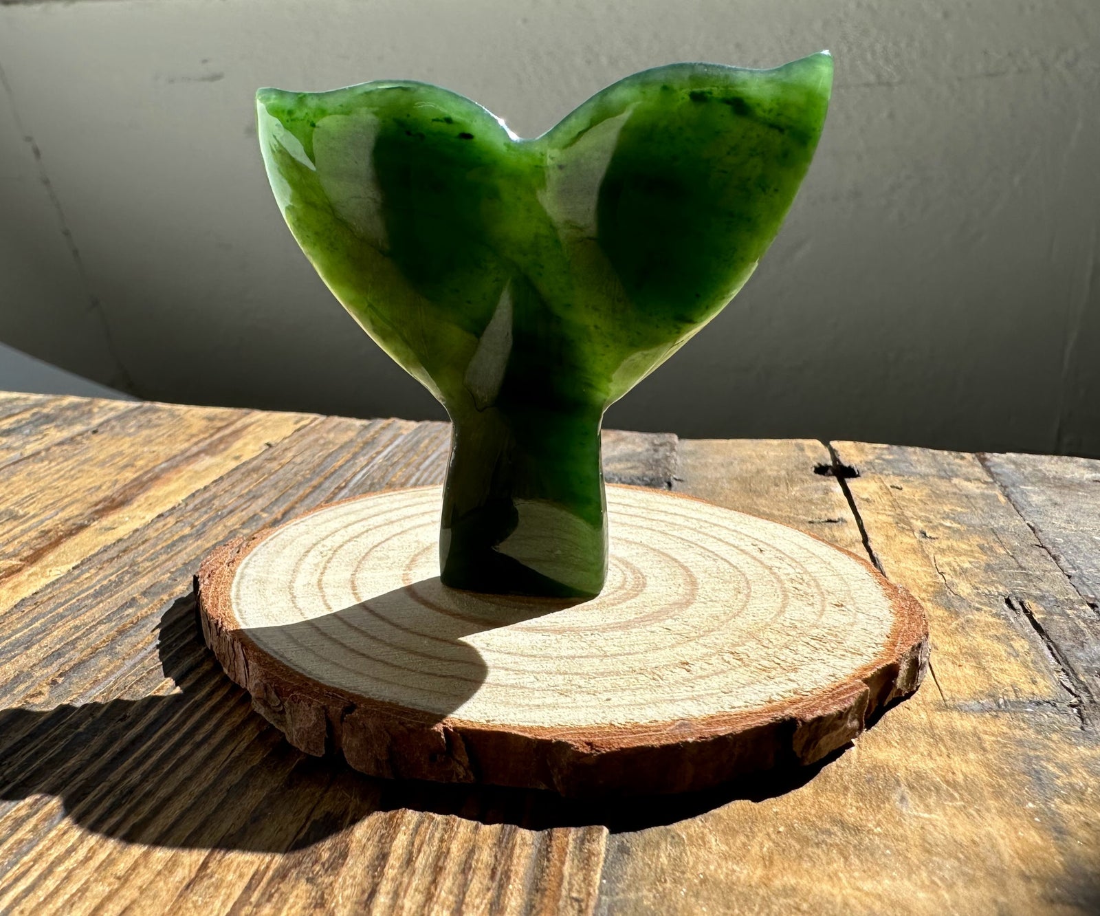 Jade whale tail sculpture in deep green mounted on a round wood base.