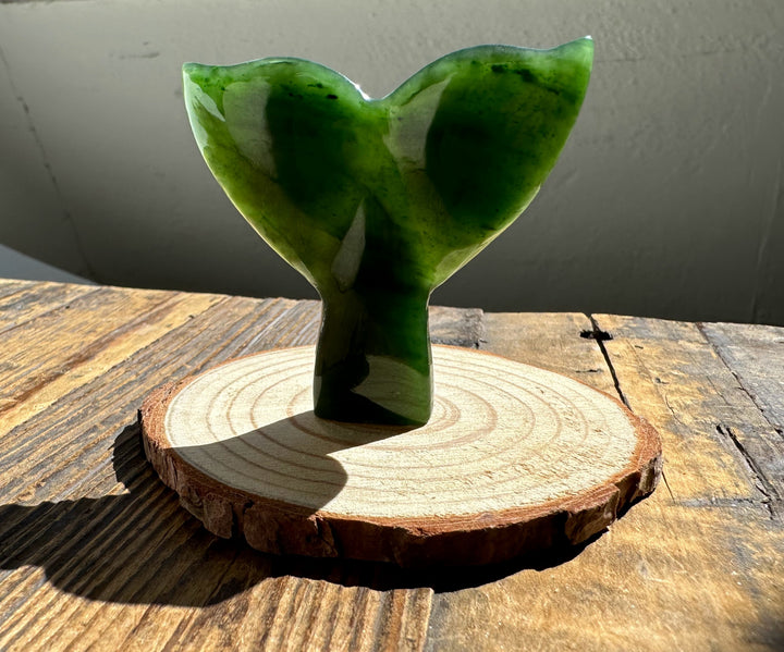 Jade whale tail sculpture in deep green mounted on a round wood base.