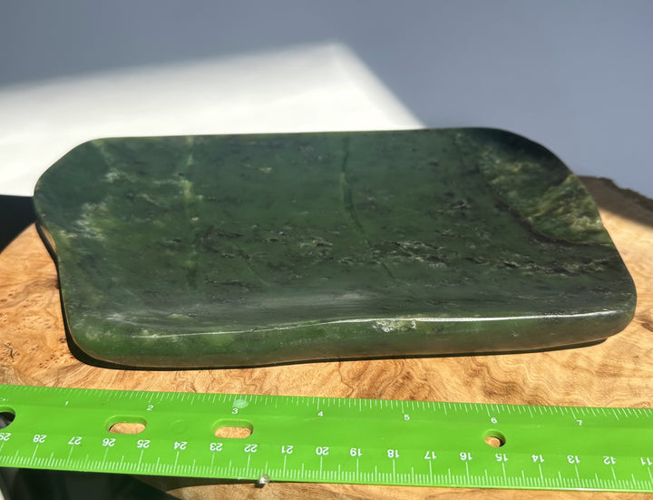 A dark green polished stone or wood plaque with rounded corners, shown on a wooden surface with a green ruler for scale.