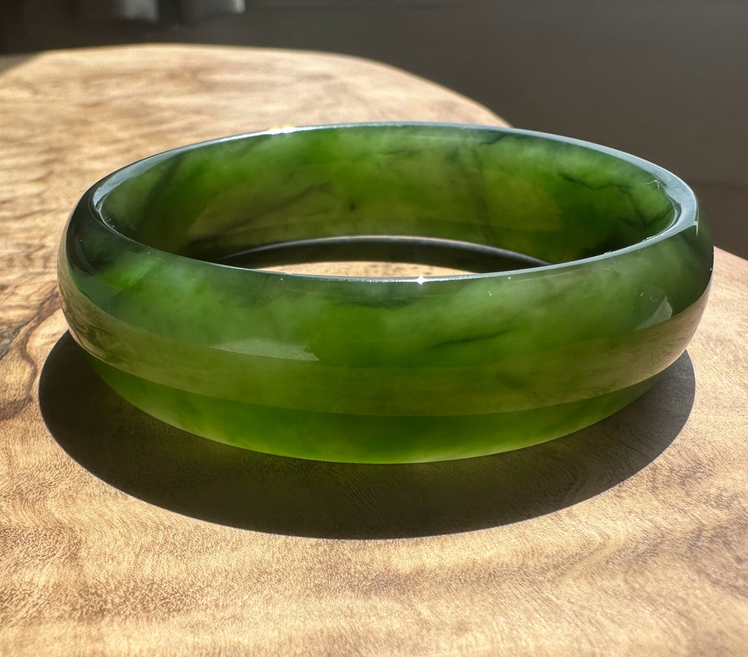 A green jade bangle bracelet with natural marbled patterns, resting on a rustic wooden surface.