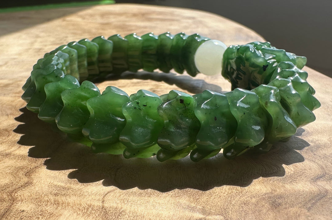 A carved green jade bracelet with a central white bead, displayed on a wooden surface.