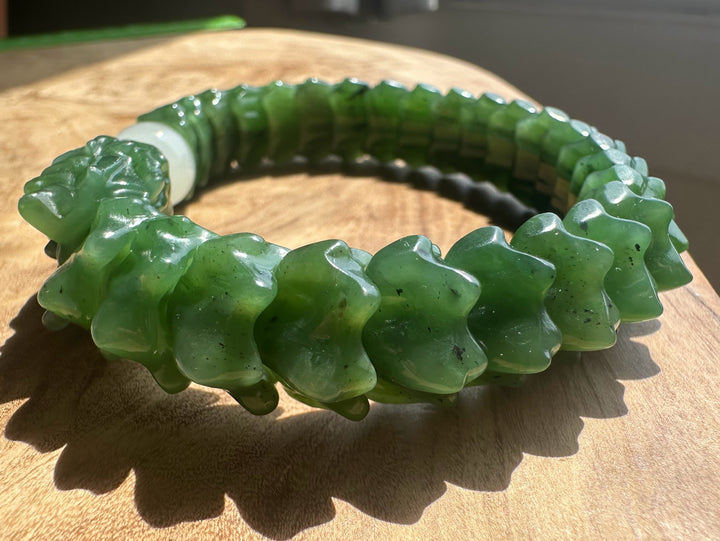 A carved green stone bracelet with a segmented, scale-like design, displayed on a wooden surface.