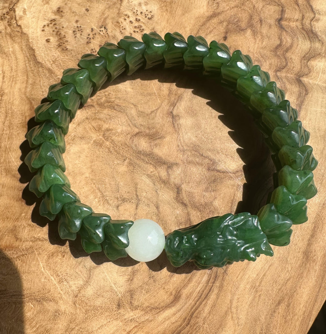 A carved green jade-like beaded bracelet with a carved animal head charm and a smooth white round bead, displayed on a wooden surface.