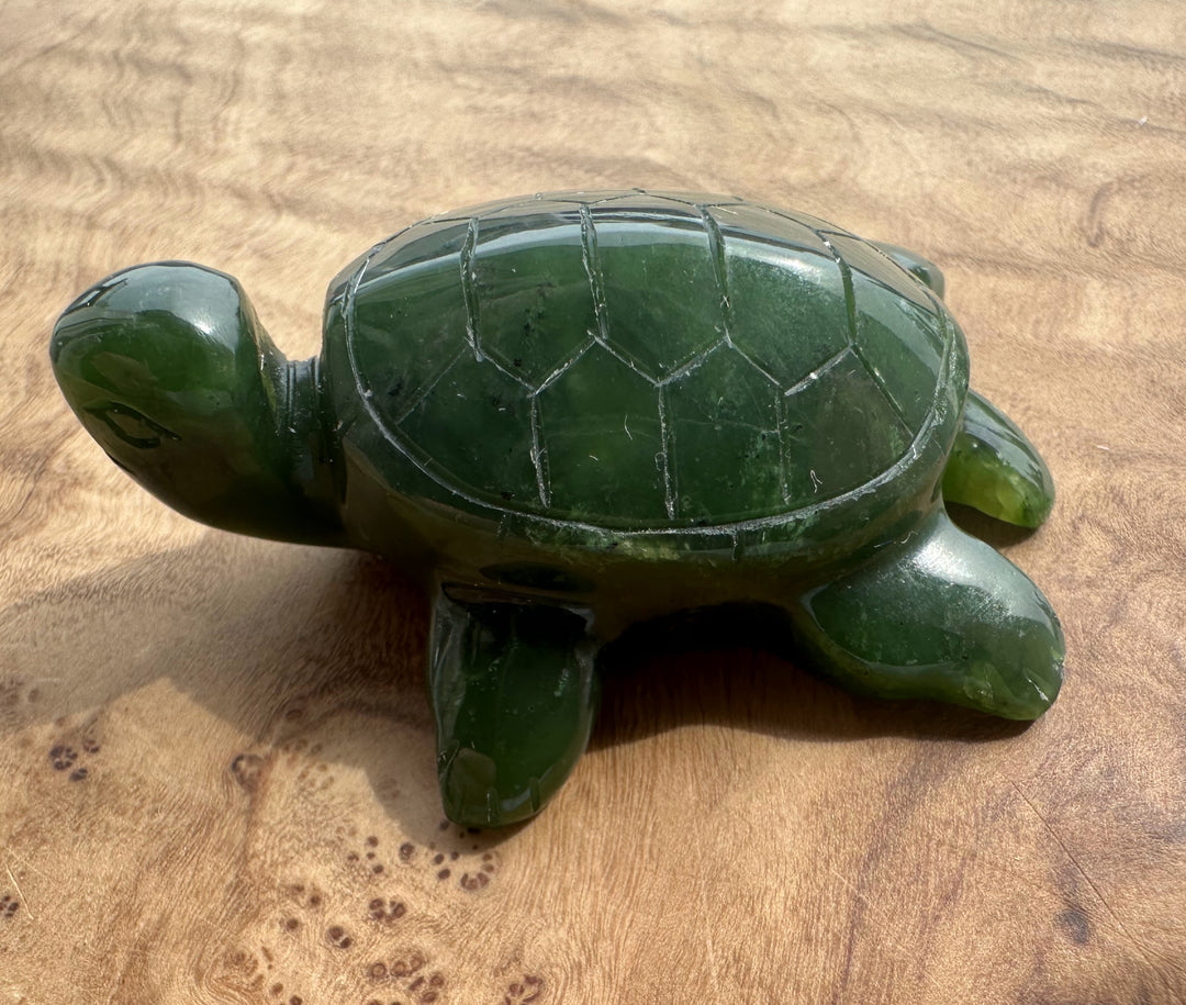 A polished dark green jade turtle figurine resting on a light brown wooden surface.
