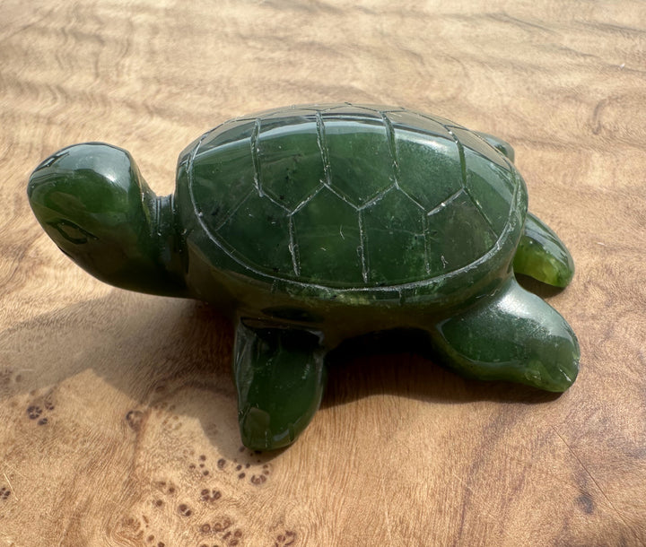 A polished dark green jade turtle figurine resting on a light brown wooden surface.