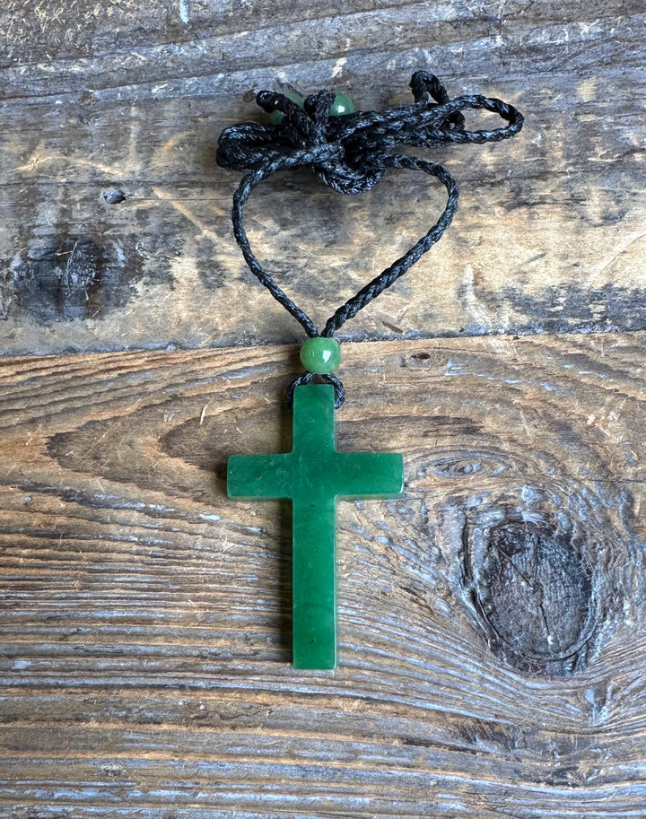 Dark green jade cross pendant on a black braided cord tied into a heart shape with a green bead above the pendant