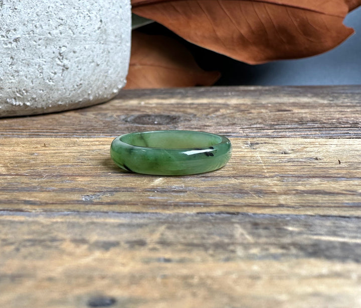 Narrow jade band ring on a rustic wooden surface with a dried brown leaf in the background