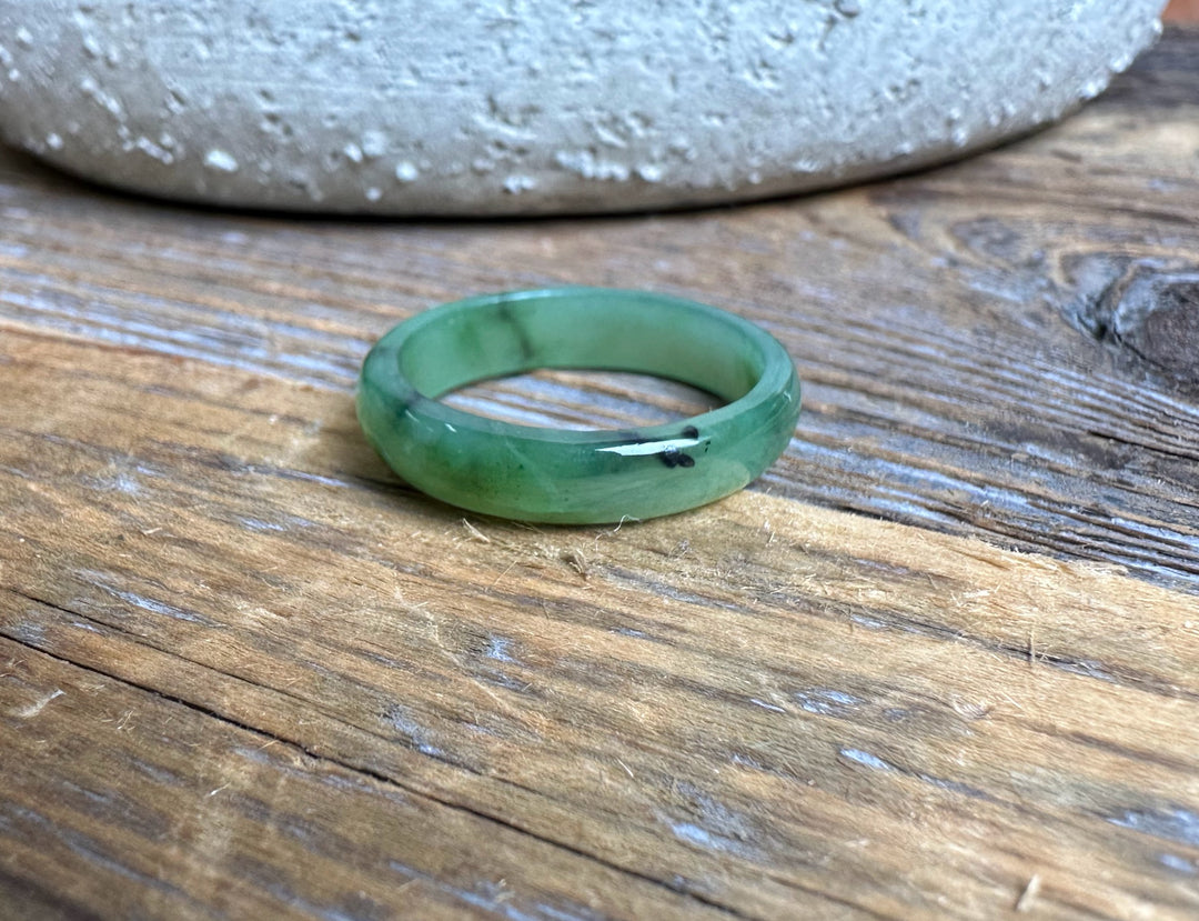 Narrow green jade band ring 5mm wide resting on a wooden surface.
