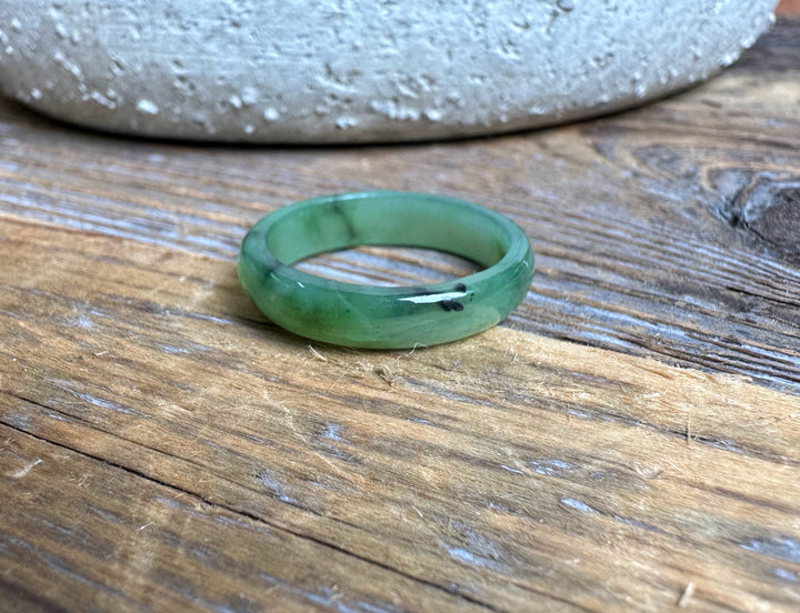 Narrow green jade band ring 5mm wide resting on a wooden surface.