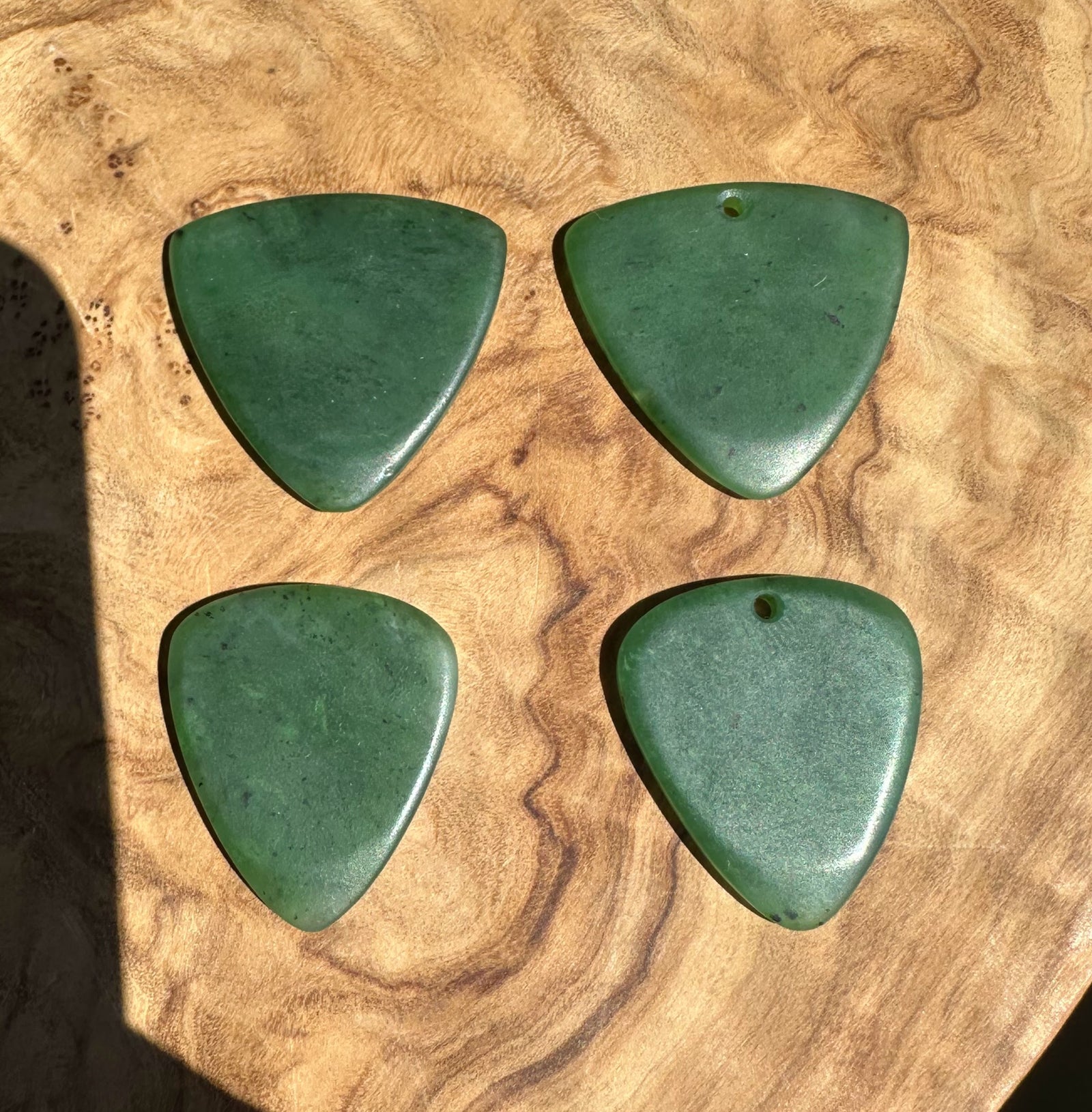 Four green jadeite guitar picks arranged in a 2x2 grid on a natural wood slice background.