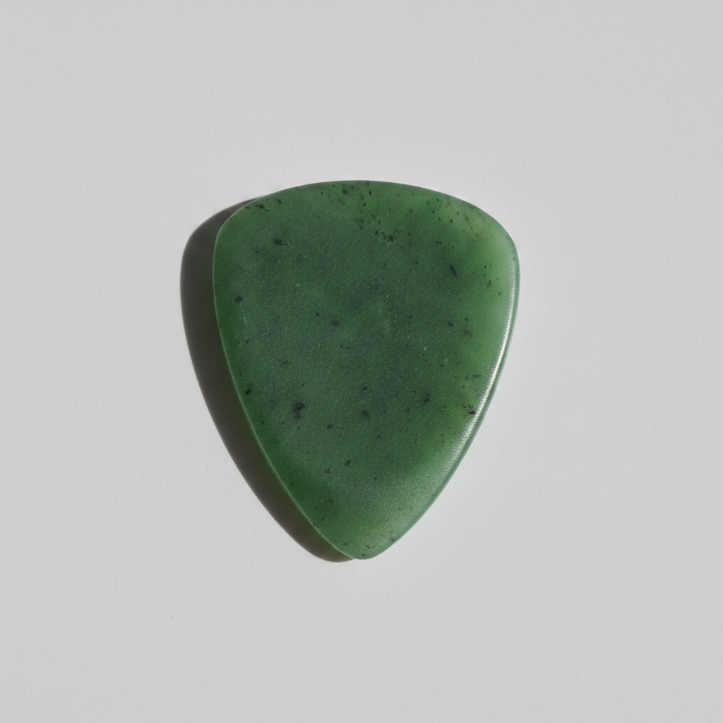 A satin finish green jade triangular guitar pick with natural speckles, resting on a grey surface