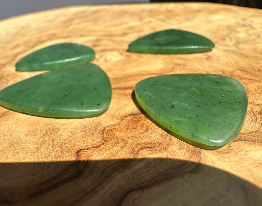 Four green polished stone guitar picks arranged on a round wooden surface.