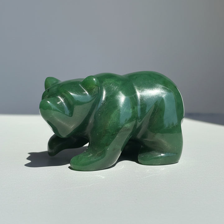 A polished green stone bear figurine standing on a round wooden surface against a neutral gray background.