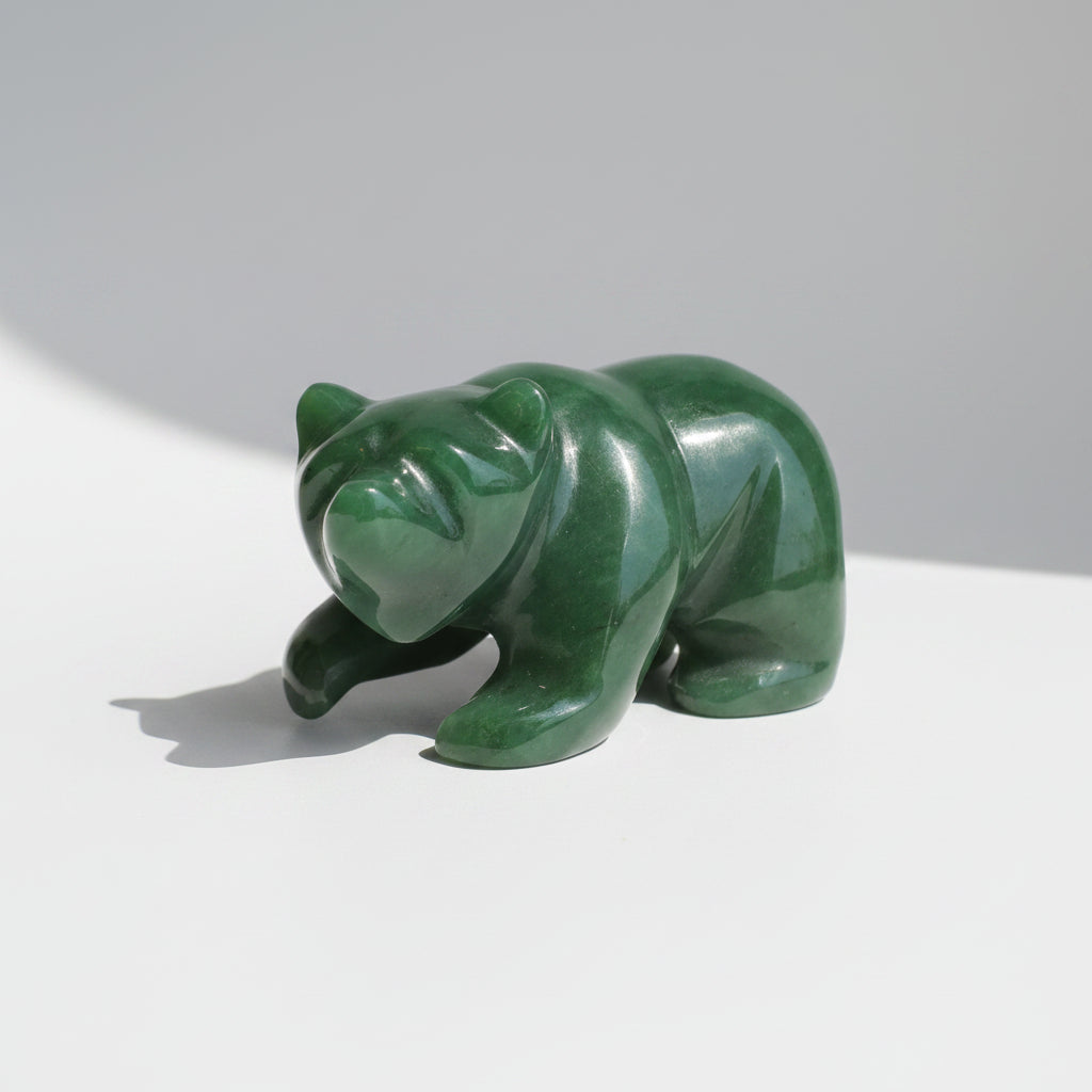 A polished green jade bear figurine resting on a wooden surface against a neutral gray background.