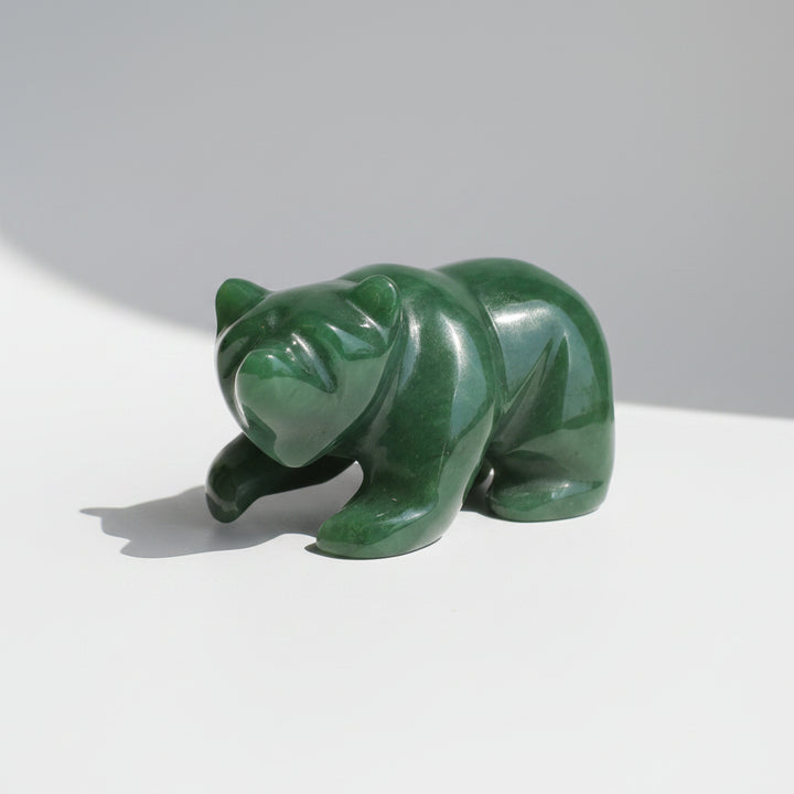 A polished green jade bear figurine resting on a wooden surface against a neutral gray background.