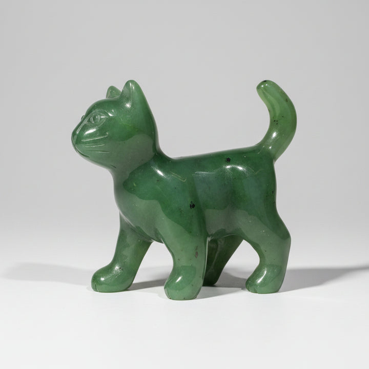 A small green translucent cat figurine standing on a round wooden surface against a neutral gray background.