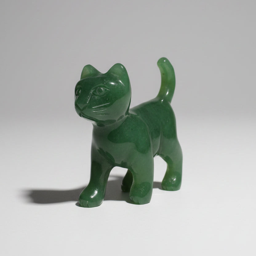 A small carved green stone cat figurine standing on a wooden surface against a plain gray background.