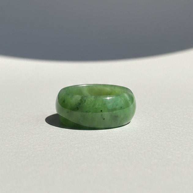 A polished green jade Ringresting on a surface with a neutral gray background.