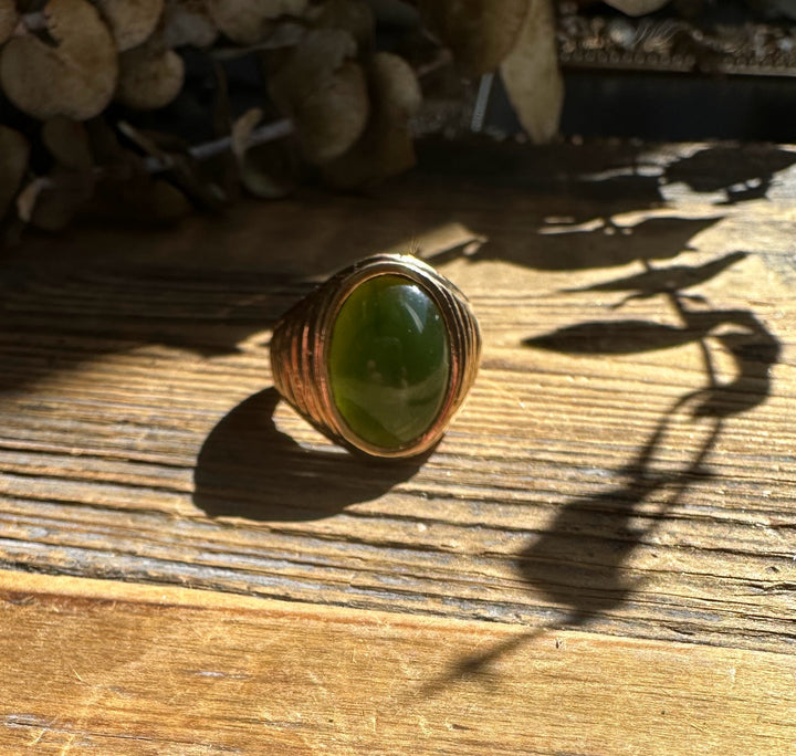 Oval green jade cabochon set in a wide copper ring with grooved sides on a wooden surface
