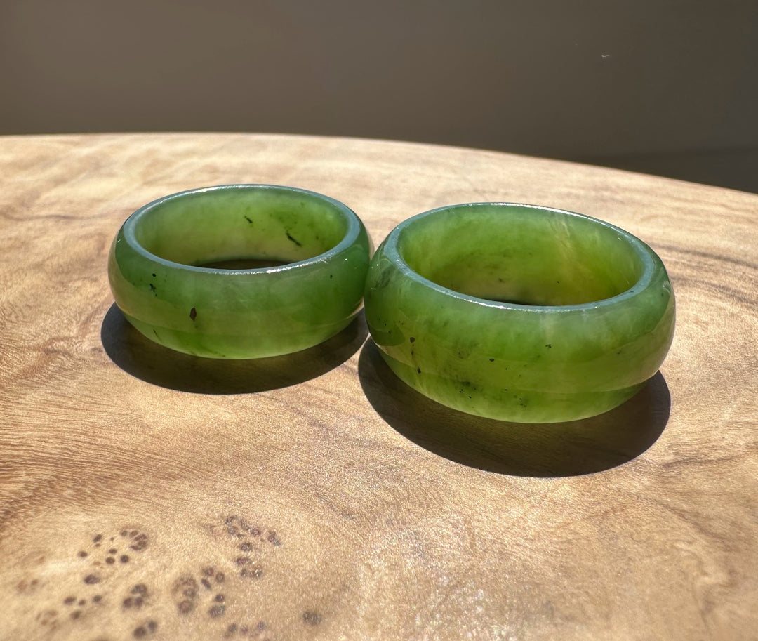 Two wide jade green bangles resting on a wooden surface.